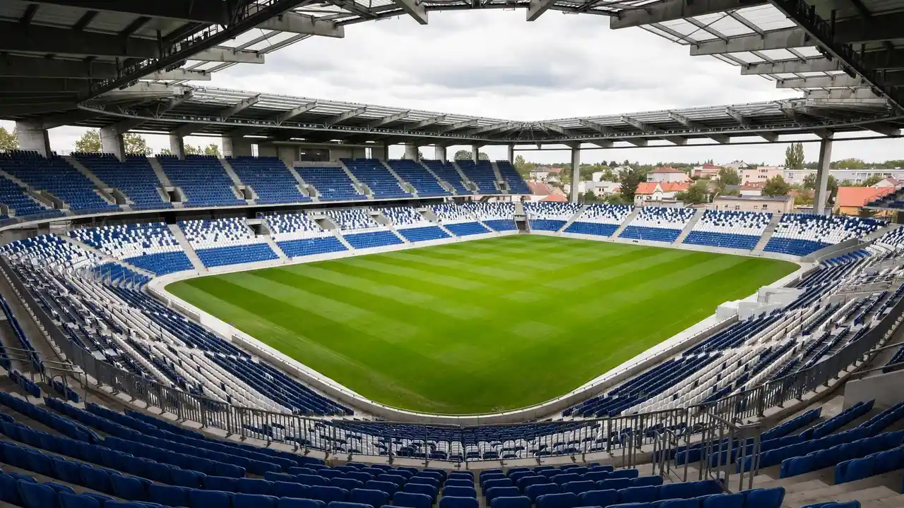 Prázdný fotbalový stadion se zeleným hřištěm a řadami sedaček.
